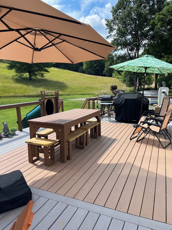 Una terraza de madera con una mesa, bancos, una parrilla y una sombrilla.