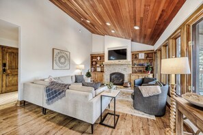 A cozy living room with a fireplace, wooden ceiling, and a television mounted above it.