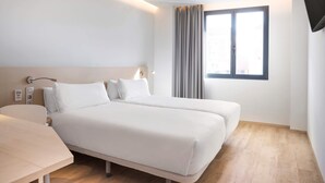 Een hotelkamer met een bed, nachtkastje, lamp en een raam met gordijnen.