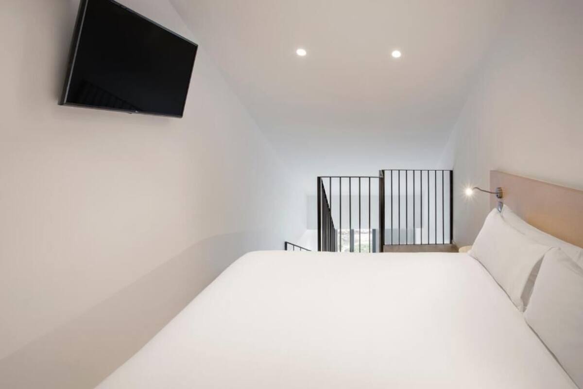A bedroom with a bed, a mounted TV, a railing, and a view of the city.