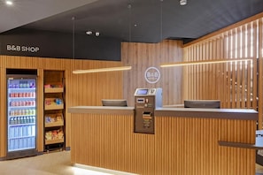A B&B shop with a wooden reception desk, a digital display, and a vending machine. - B&B Hotel Málaga Centro (Málaga)