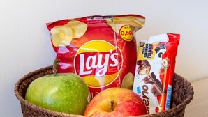 Ein Korb mit Lay's Kartoffelchips, einer Schokoladenriegel und zwei Äpfeln.