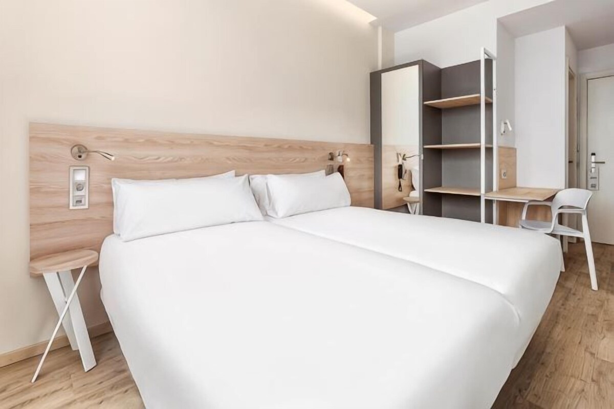 A modern hotel room with a large bed, a desk, and a chair.