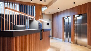 Een moderne receptie met een houten balie, een trap en twee liften.