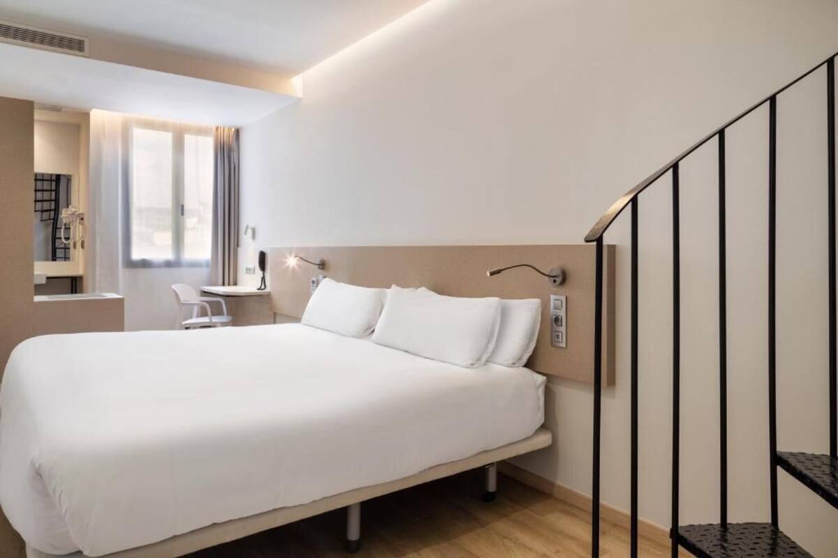 A hotel room with a bed, a desk, a chair, and a staircase.