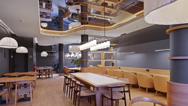 Een modern restaurantinterieur met houten tafels, comfortabele zitplaatsen en moderne verlichtingsarmaturen.