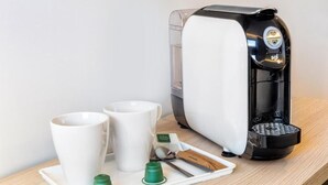 Eine Kaffeemaschine mit zwei weißen Tassen und einer Tablett mit grünen Kapseln und einem Löffel auf einer Holzoberfläche.