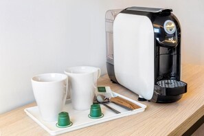 Eine Kaffeemaschine mit zwei weißen Tassen und einer Tablett mit grünen Kapseln und einem Löffel auf einer Holzoberfläche.