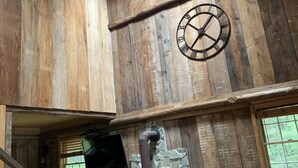 Un intérieur rustique avec des murs en bois, une cheminée en pierre, une table à manger avec des chaises et un ventilateur de plafond.