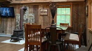 Un intérieur rustique avec des murs en bois, une cheminée en pierre, une table à manger en bois avec des chaises et une grande horloge murale.