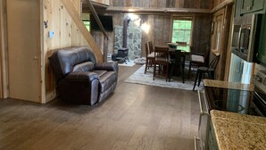 Un intérieur de chalet chaleureux avec un canapé en cuir, une table à manger, des chaises, une cheminée en pierre et un coin cuisine.