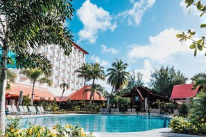 A hotel with a swimming pool, palm trees, and a red-roofed building.