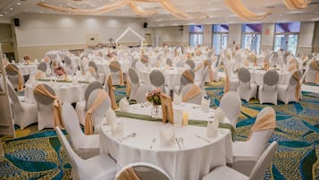A banquet hall with round tables, white chairs, and a patterned carpet.