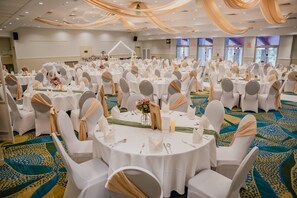 Une salle de banquet avec des tables rondes, des chaises blanches et un tapis à motifs.