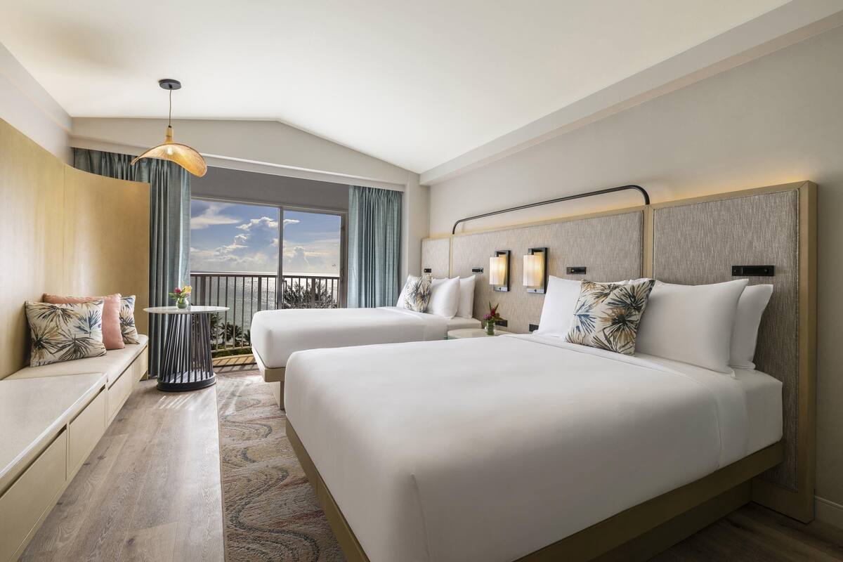 A hotel room with two beds, a sofa, a round table, and a balcony with a view.