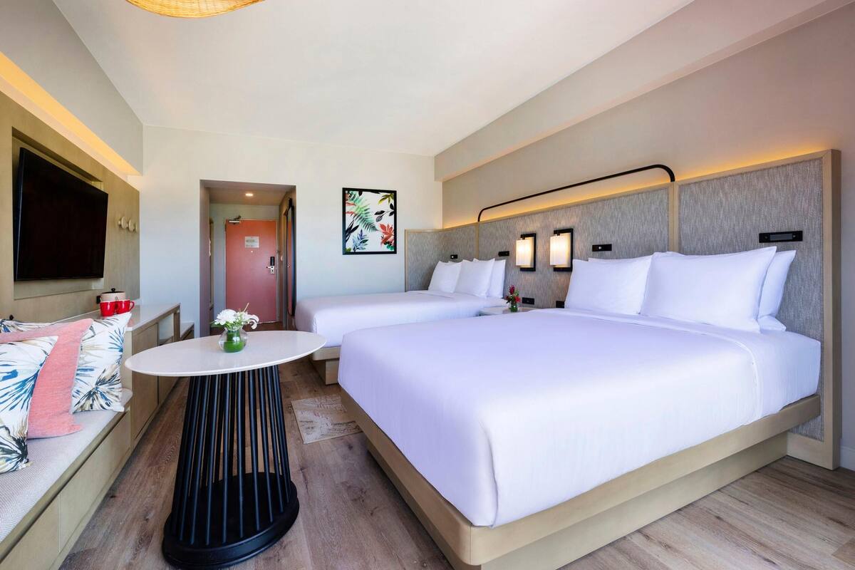 A hotel room with two beds, a round table, a TV, and a door leading to another room.