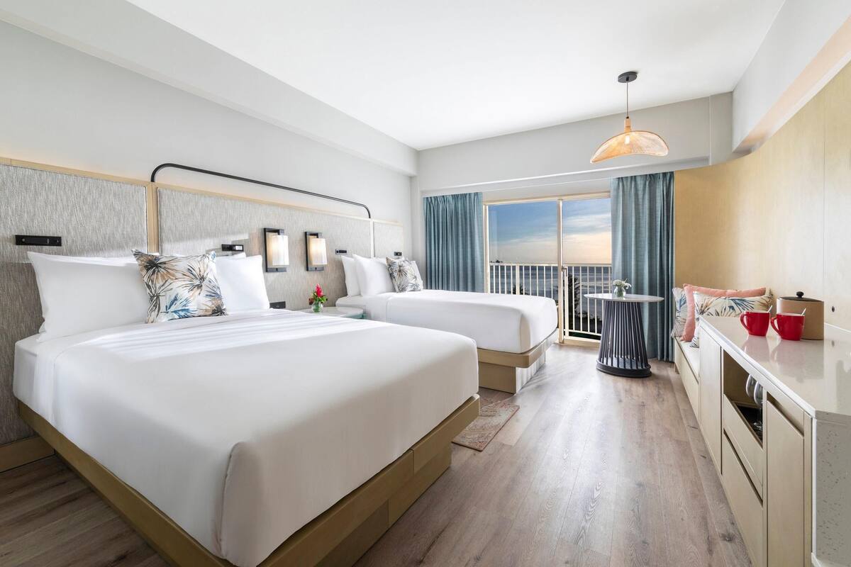 A hotel room with two beds, a balcony, a dining area, and a view of the sky.