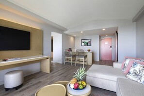 Una sala de estar moderna con un televisor de pantalla plana, un comedor con sillas, un sofá y un frutero sobre una mesita.