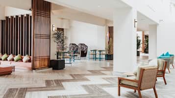 A spacious lobby with a herringbone floor pattern, a seating area with wicker chairs and a sofa, and a wooden partition with vertical slats.