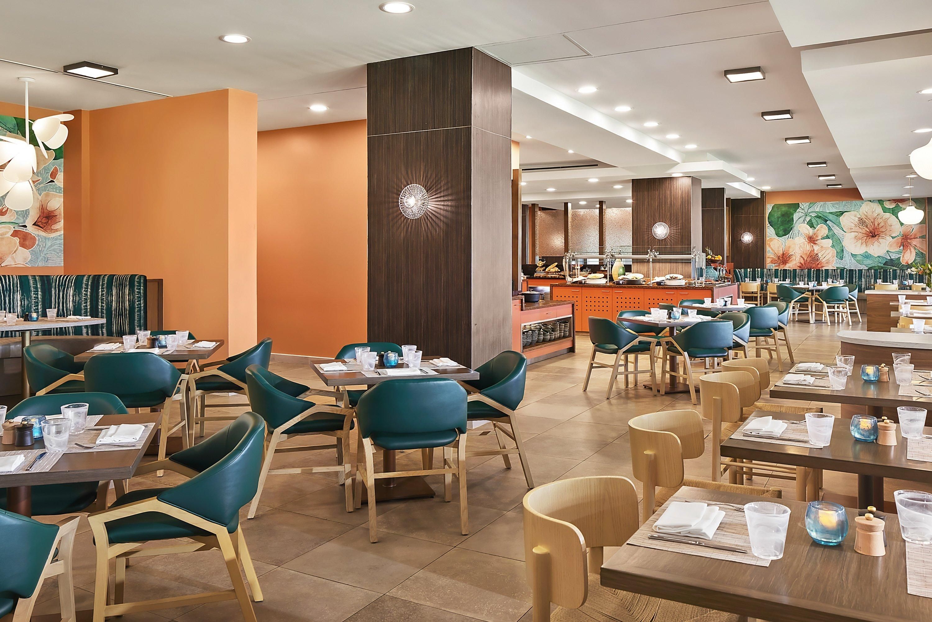 A spacious restaurant with multiple dining tables and chairs, a counter with a cash register, and a decorative wall mural.