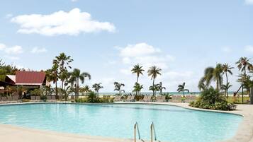 A swimming pool with lounge chairs, palm trees, and a building with a red roof.