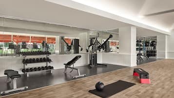 Un gimnasio con equipo de ejercicio, bancos y piso de madera.