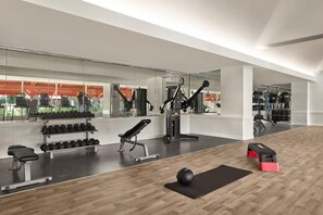 Un gimnasio con equipo de ejercicio, bancos y piso de madera.