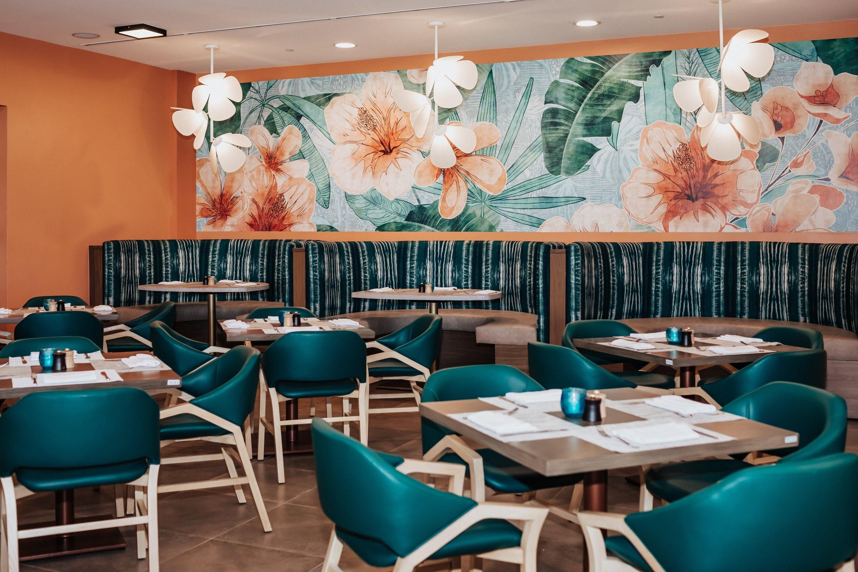 Un restaurante con sillas color turquesa, mesas de madera y un mural floral en la pared.