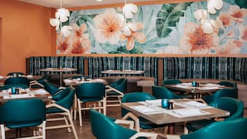 Un restaurante con sillas color turquesa, mesas de madera y un mural floral en la pared.