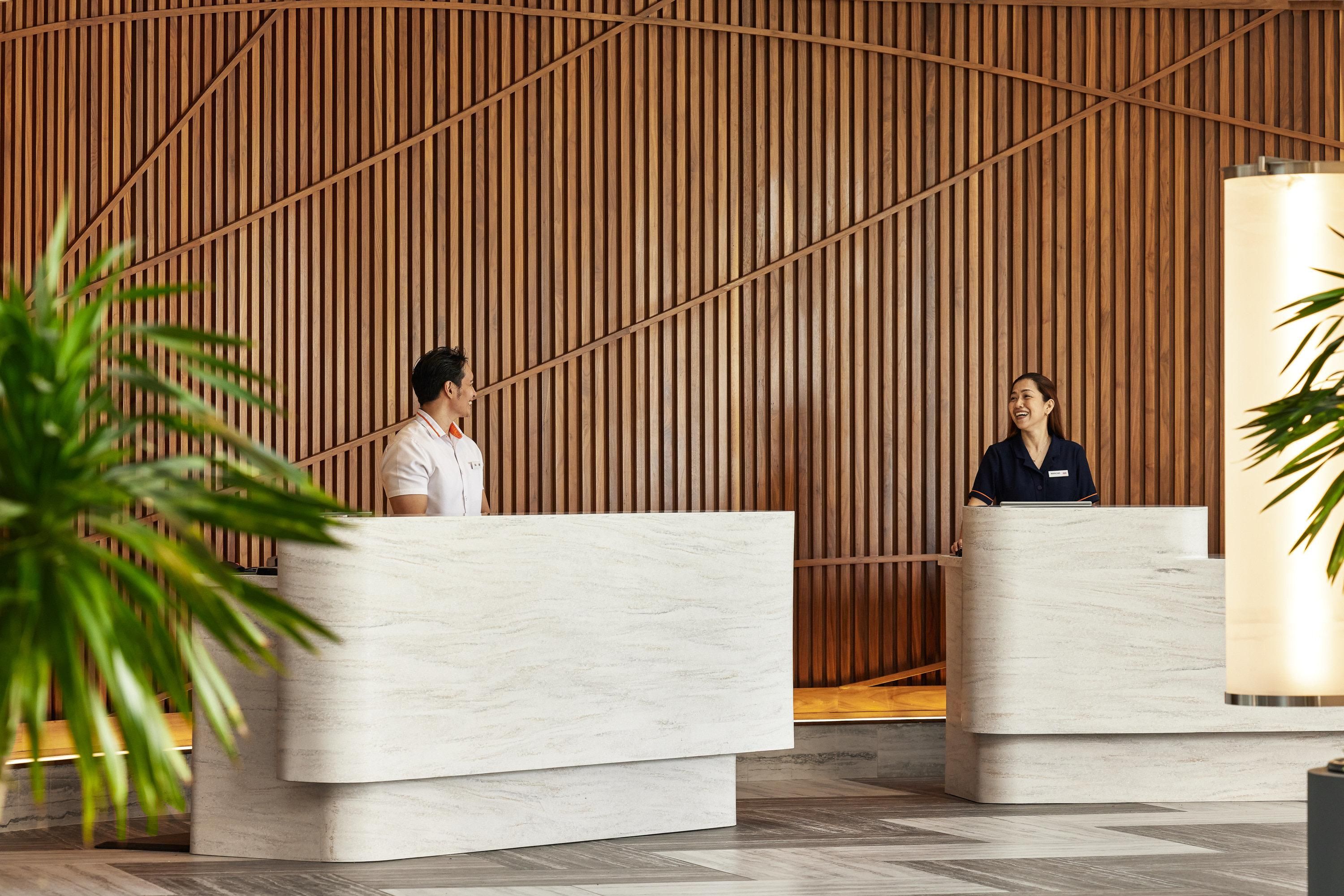 A reception area with two marble reception desks, wooden slat wall, and potted plants.