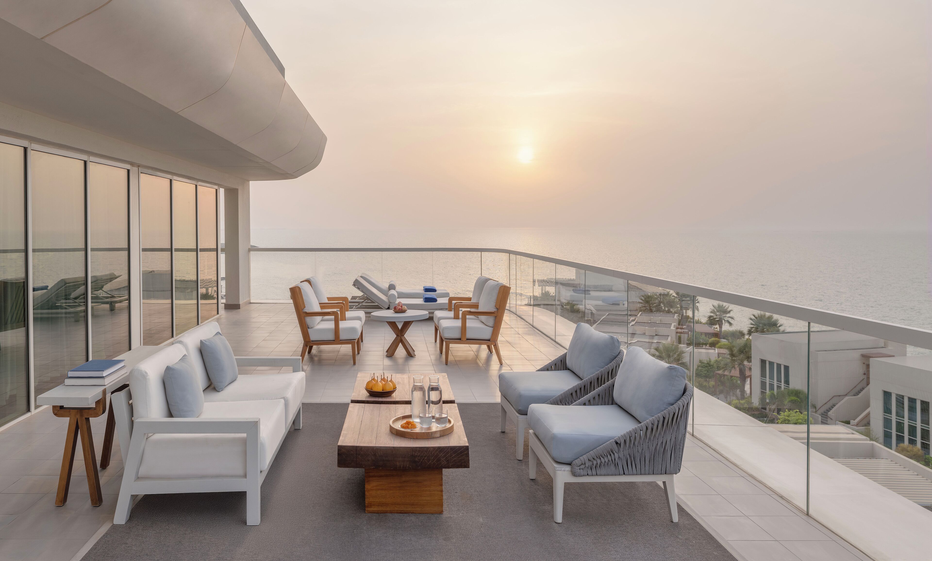 A modern outdoor seating area with a view of the sea, featuring a sofa, chairs, and a coffee table.