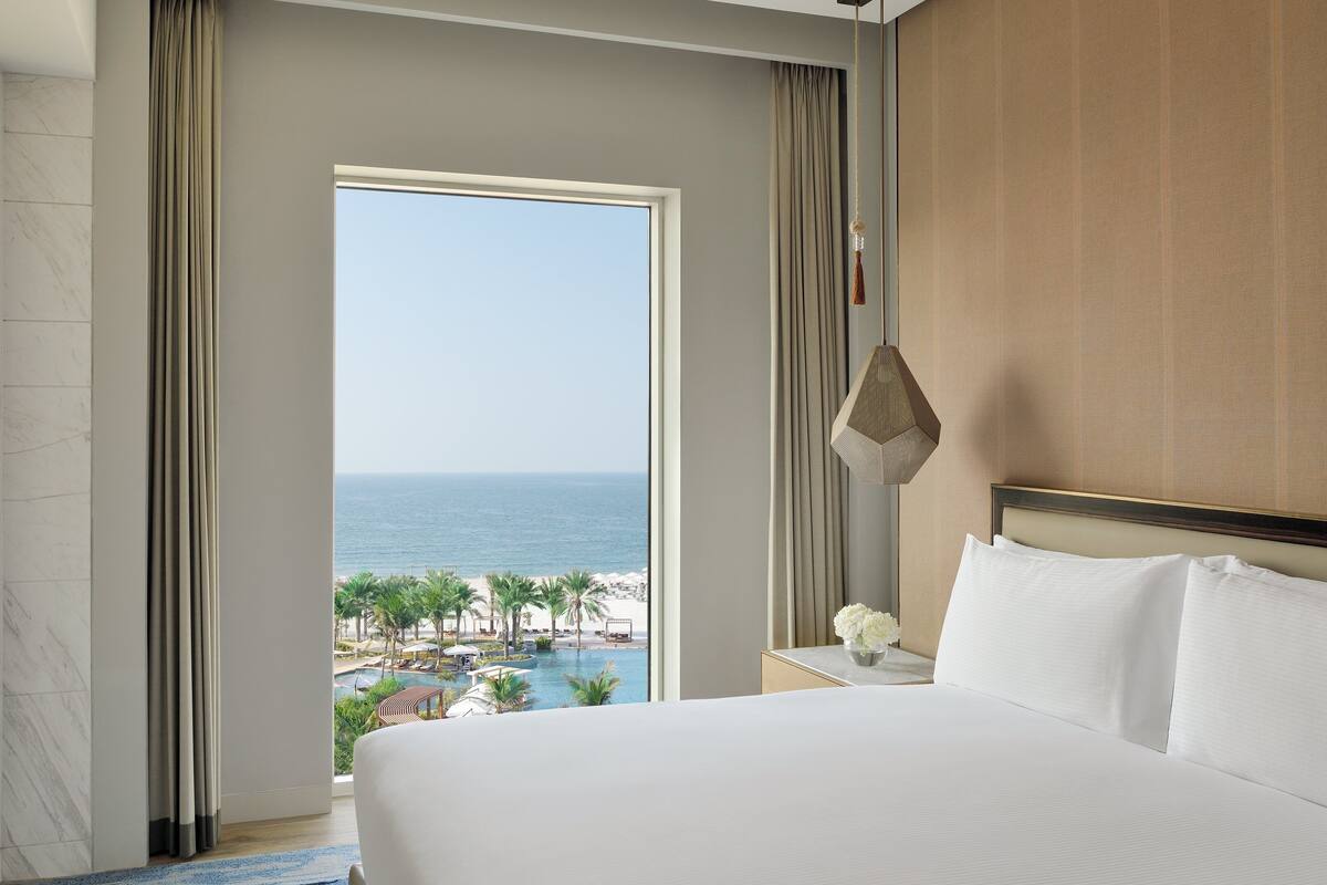 A hotel room with a large bed, a TV, a view of the ocean, and a pool.