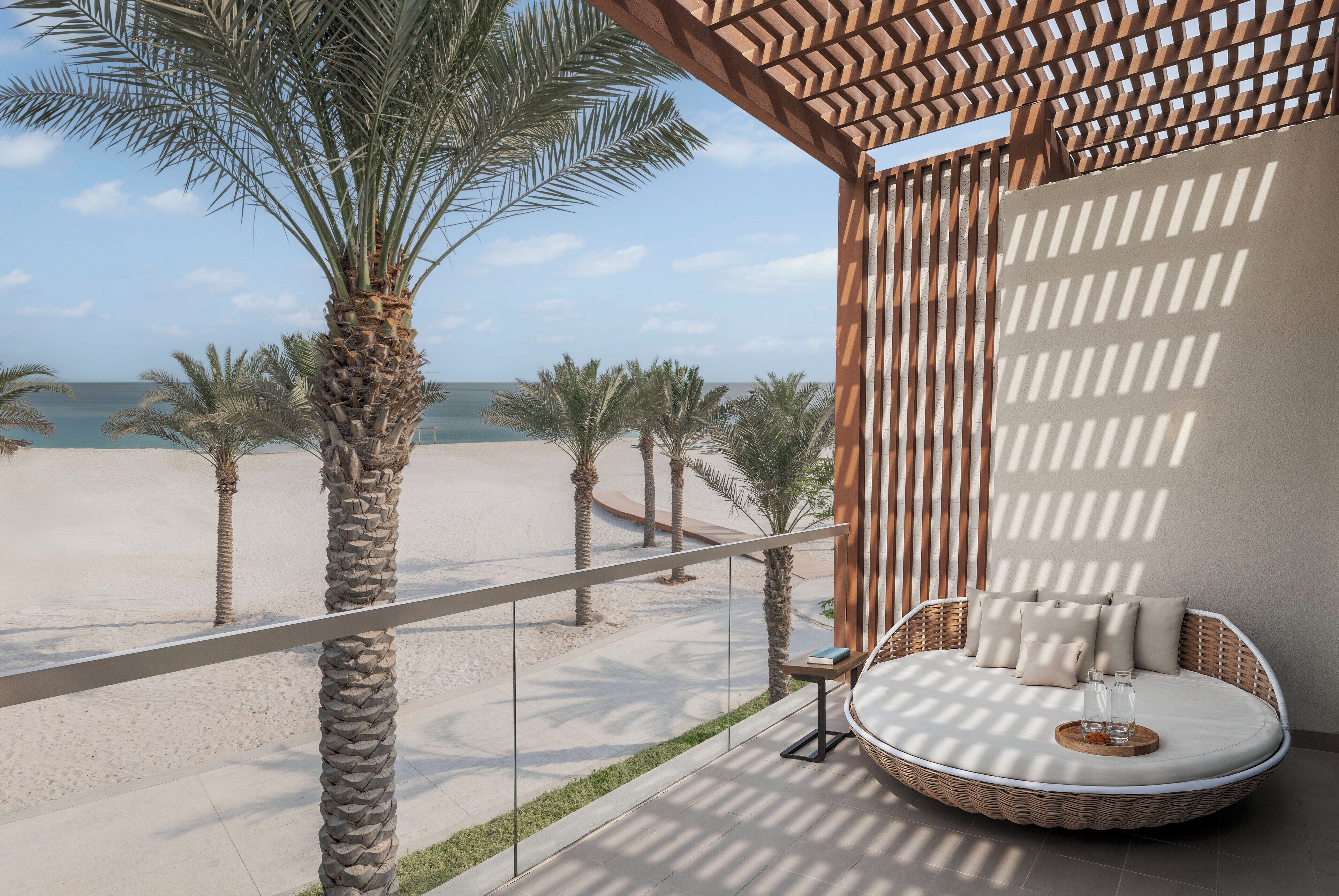 A balcony with a wicker sofa, a small table, and a view of the beach and ocean.