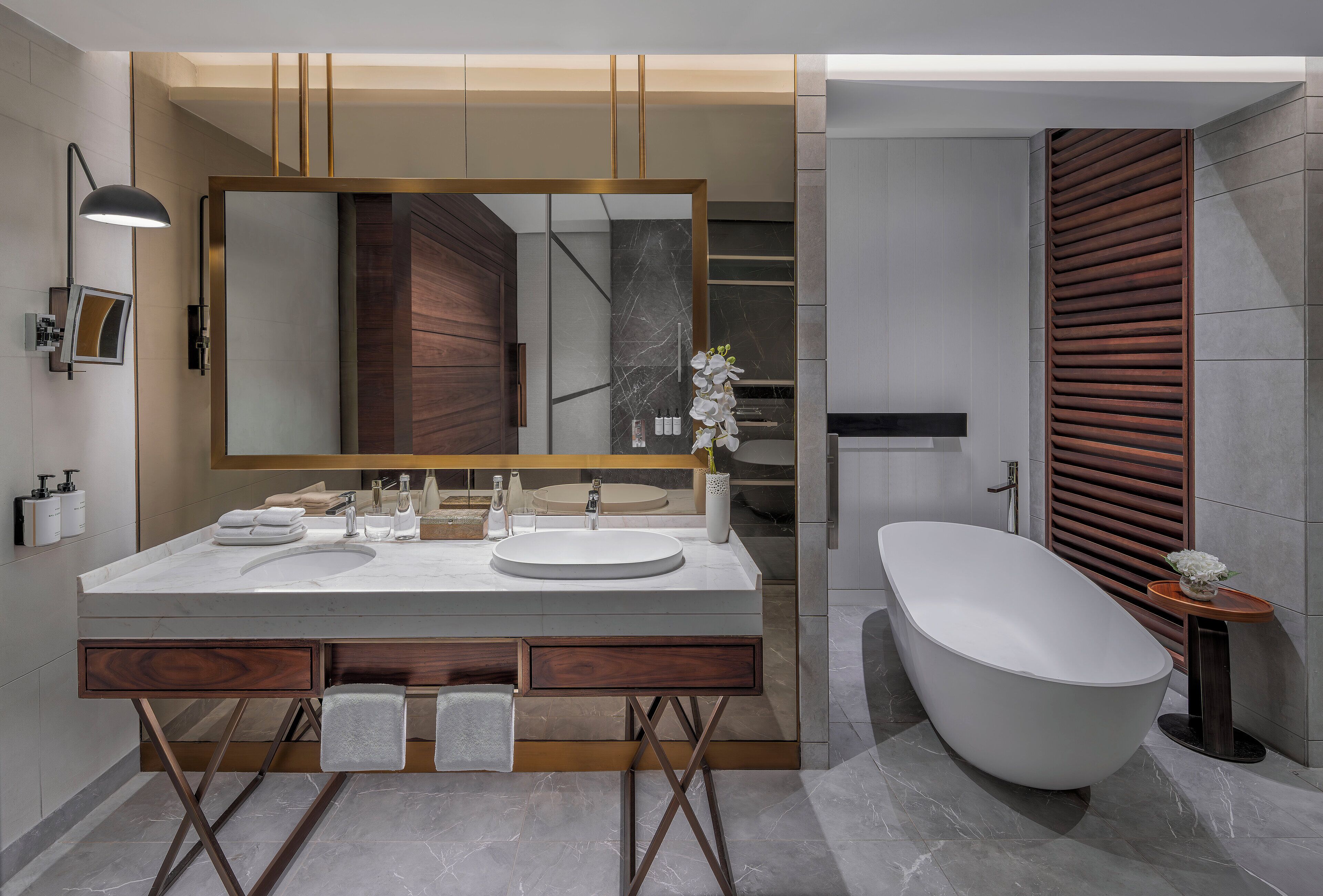 A modern bathroom with a large mirror, two sinks, a freestanding bathtub, and wooden accents.