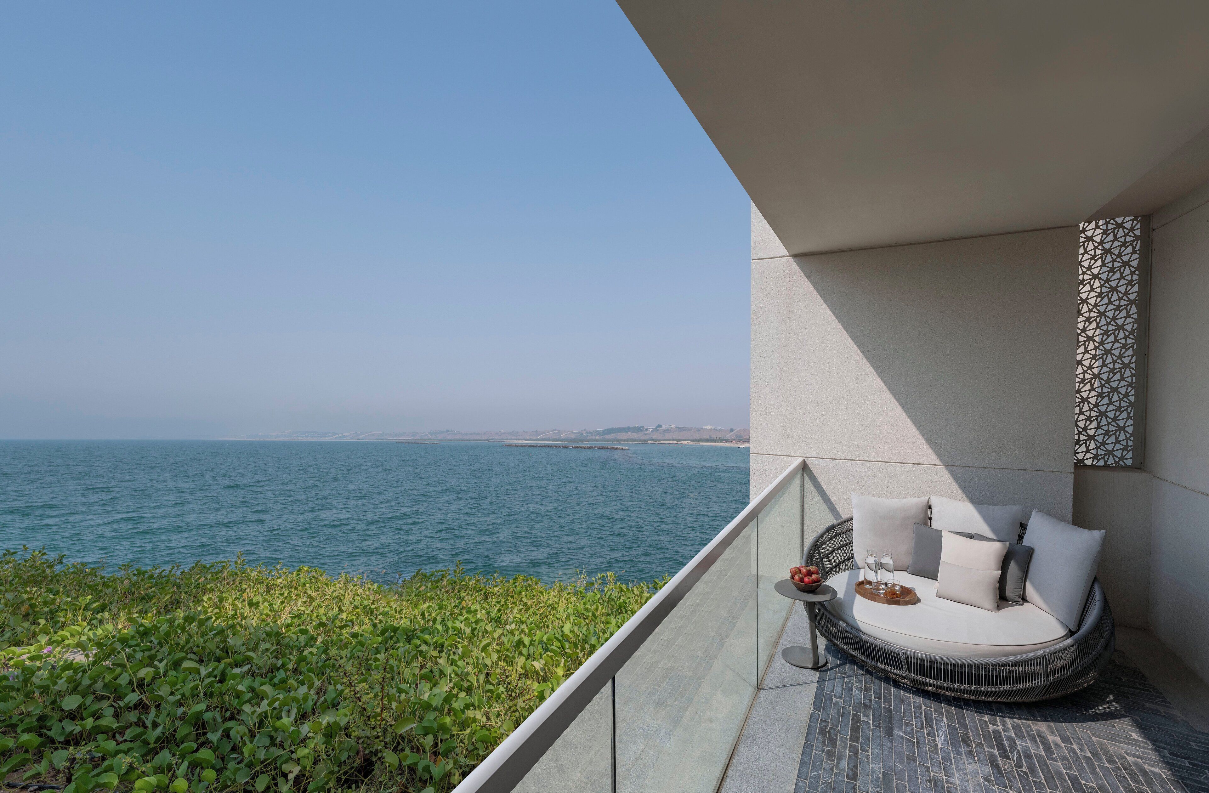Un balcón con una zona de estar con cojines blancos, una mesita con bandeja y vistas al mar.