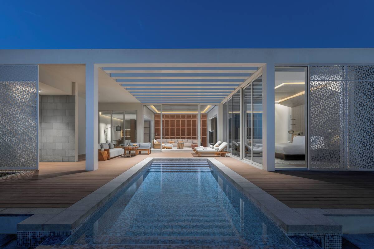 A modern outdoor pool area with a wooden deck, lounge chairs, and a glass-enclosed bedroom.