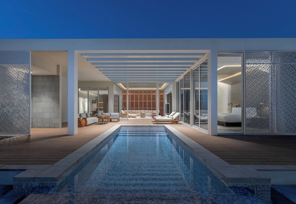 A modern outdoor pool area with a wooden deck, lounge chairs, and a glass-enclosed bedroom.