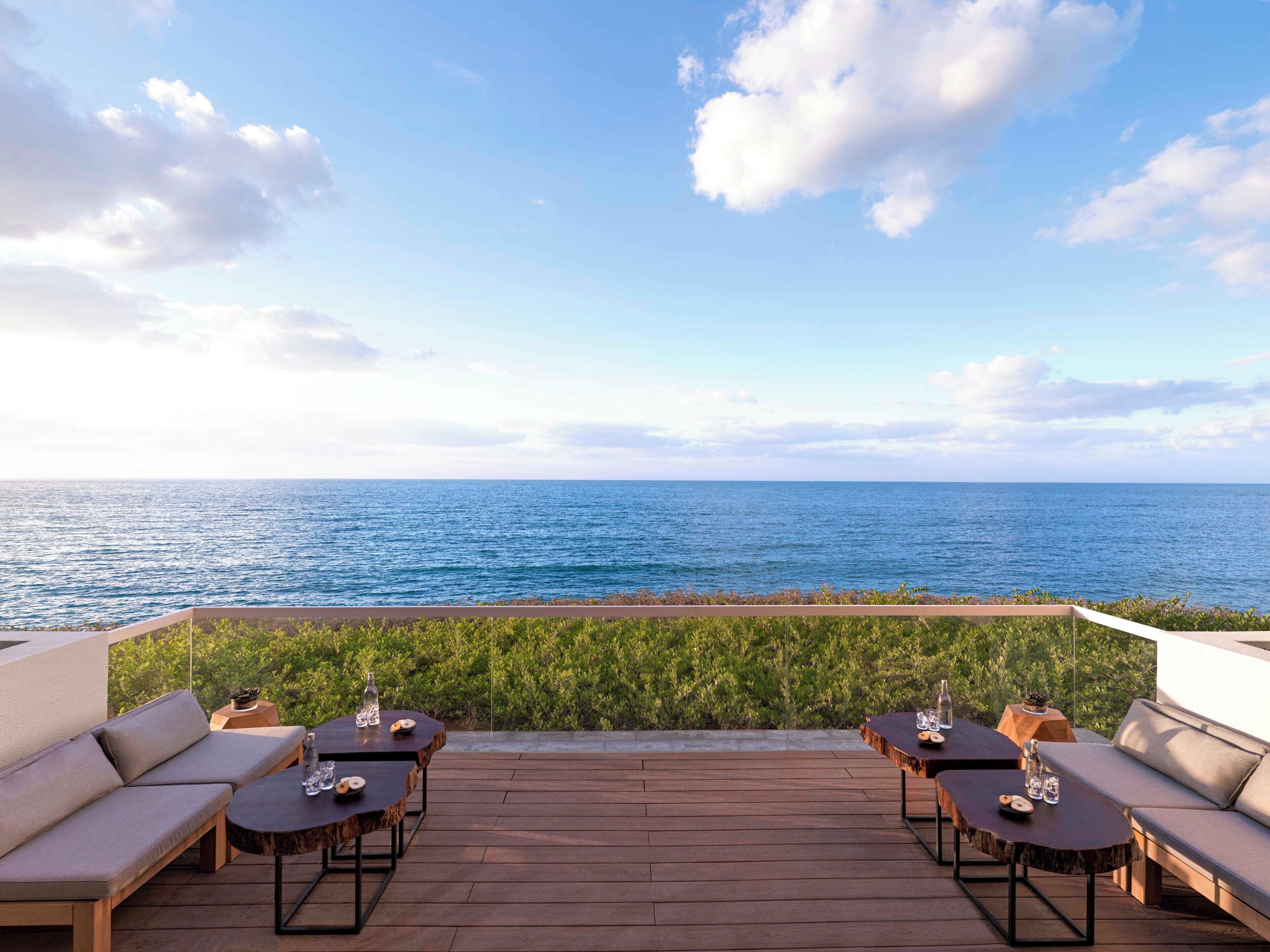 Ein Sitzbereich im Freien mit Blick auf das Meer, ausgestattet mit Holztischen und Sofas.