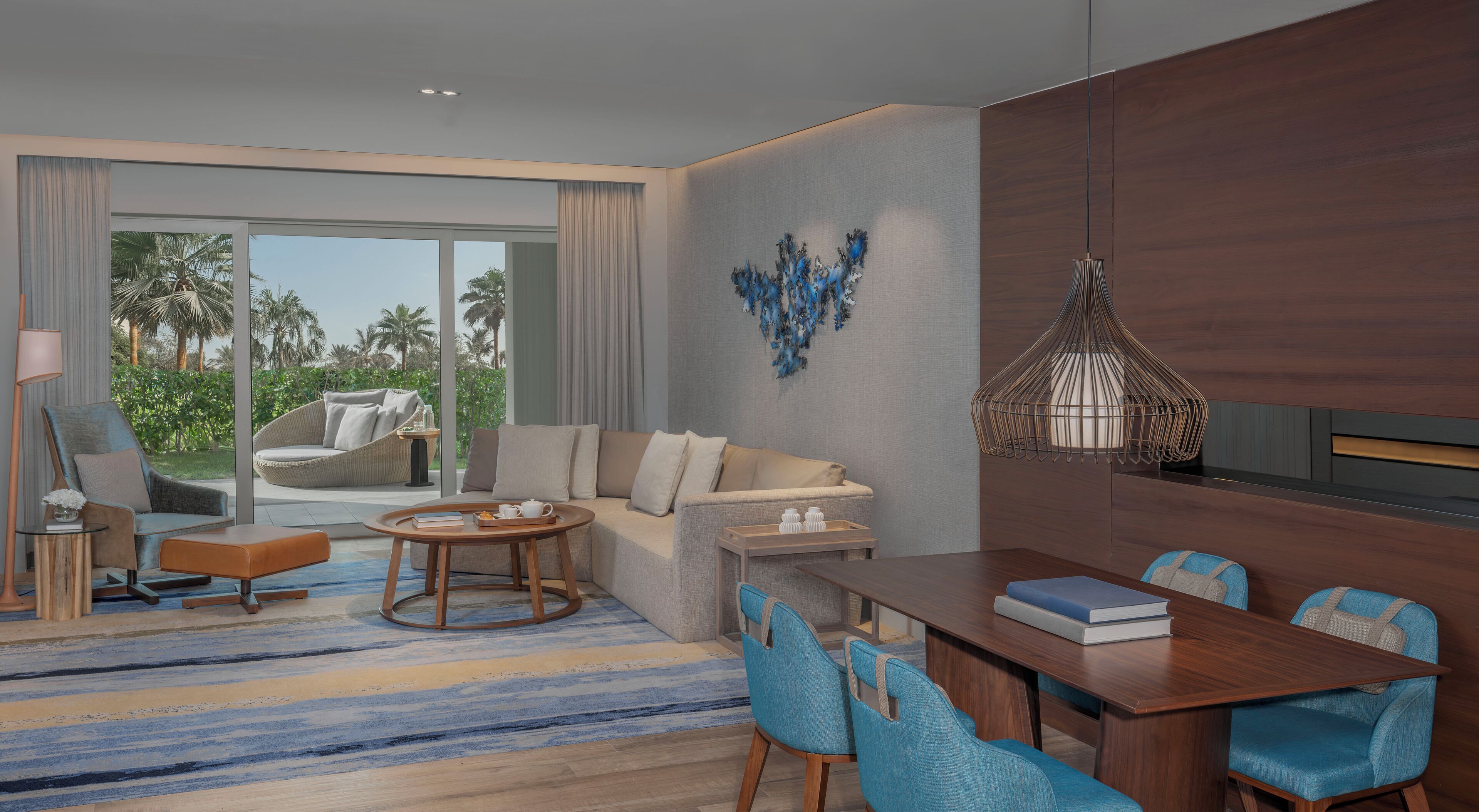 Une chambre d’hôtel moderne avec un canapé, une table à manger, des chaises et une vue sur des palmiers.