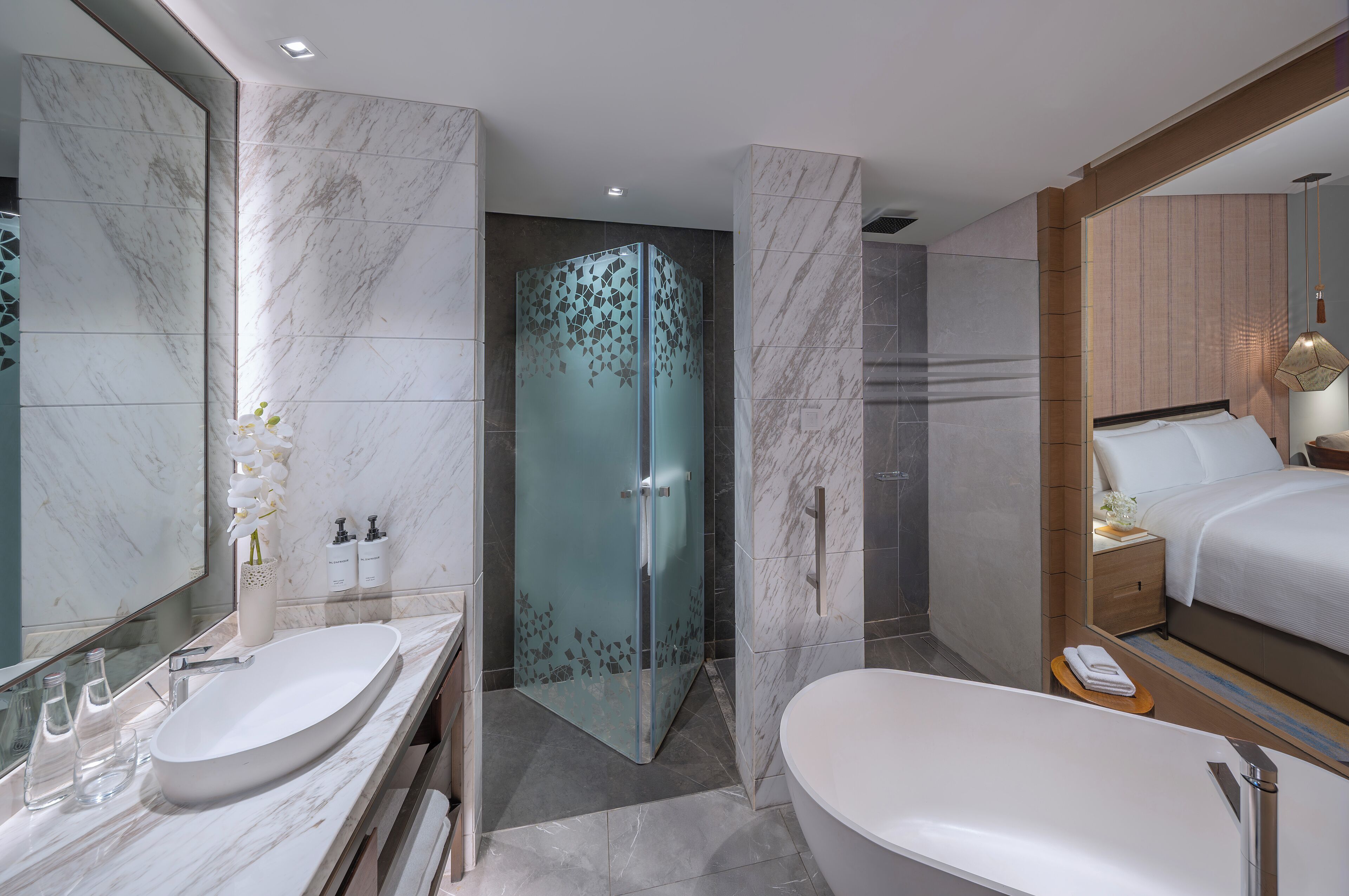 Un baño moderno con un espejo grande, una bañera independiente, una ducha con cerramiento de vidrio y un tocador con un lavamanos y dos botellas de champú.