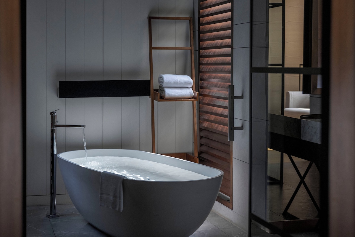 A modern bathroom with a freestanding bathtub, a wooden ladder shelf, and a minimalist design.