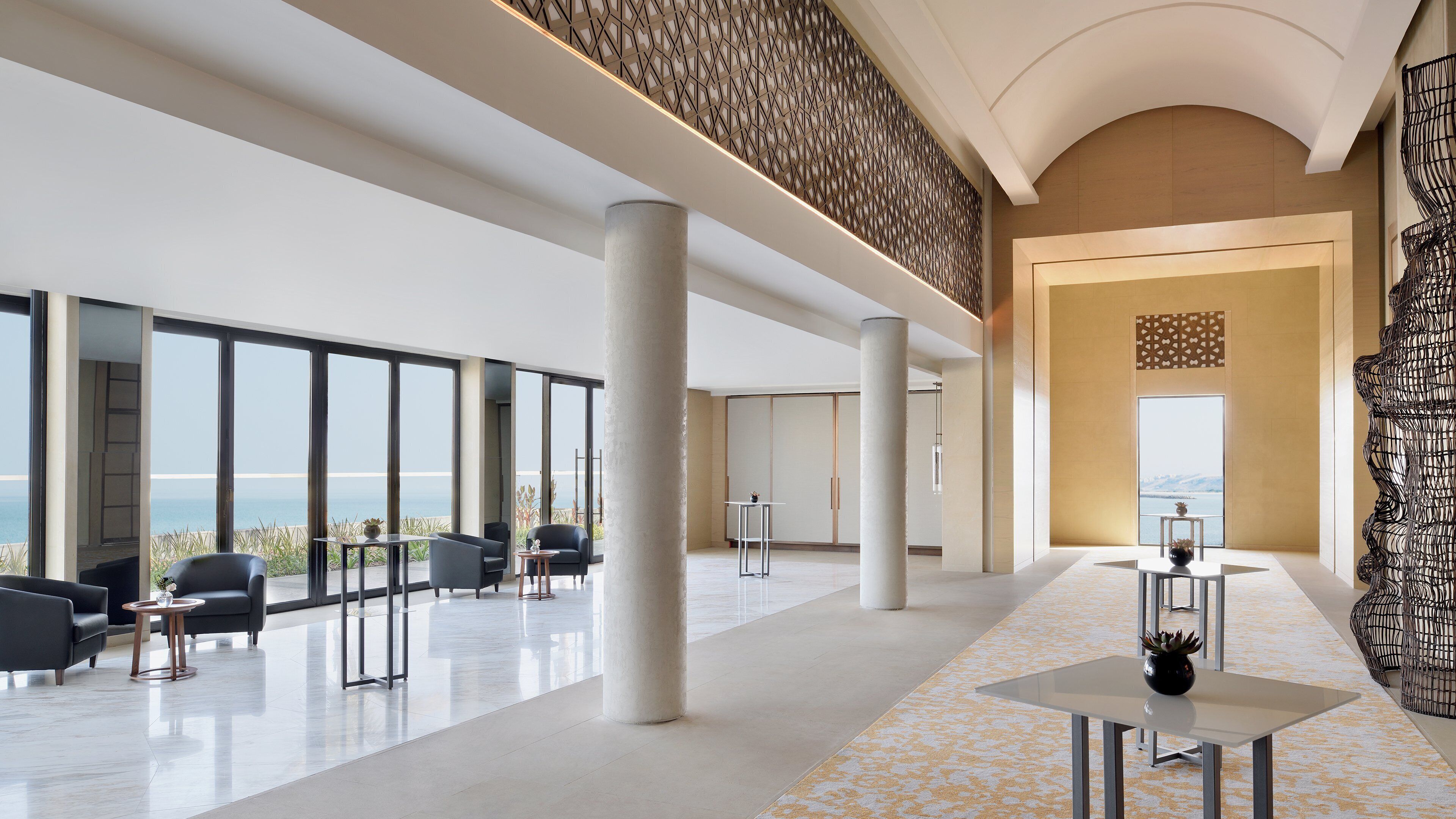 A spacious lobby with large windows, a high ceiling, and a view of the sea.