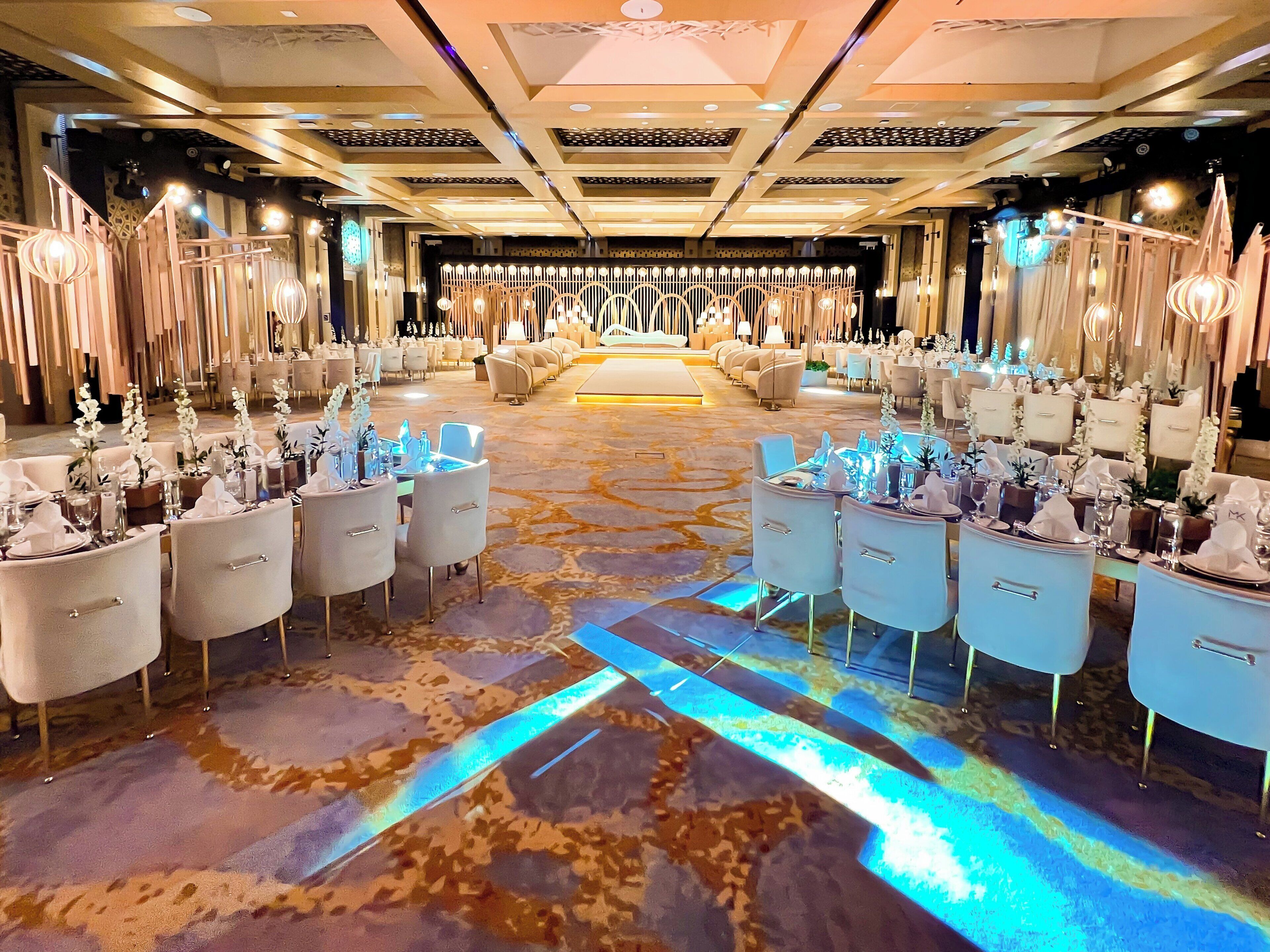 A spacious hotel lobby with a central seating area, multiple dining tables, and a patterned carpet.