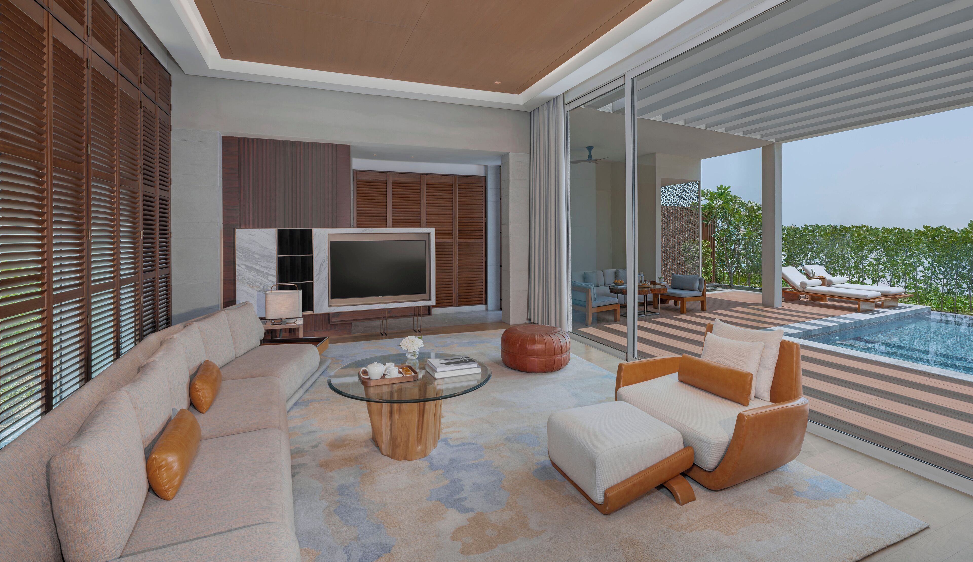 A modern living room with a flat-screen TV, comfortable seating, and a pool area.