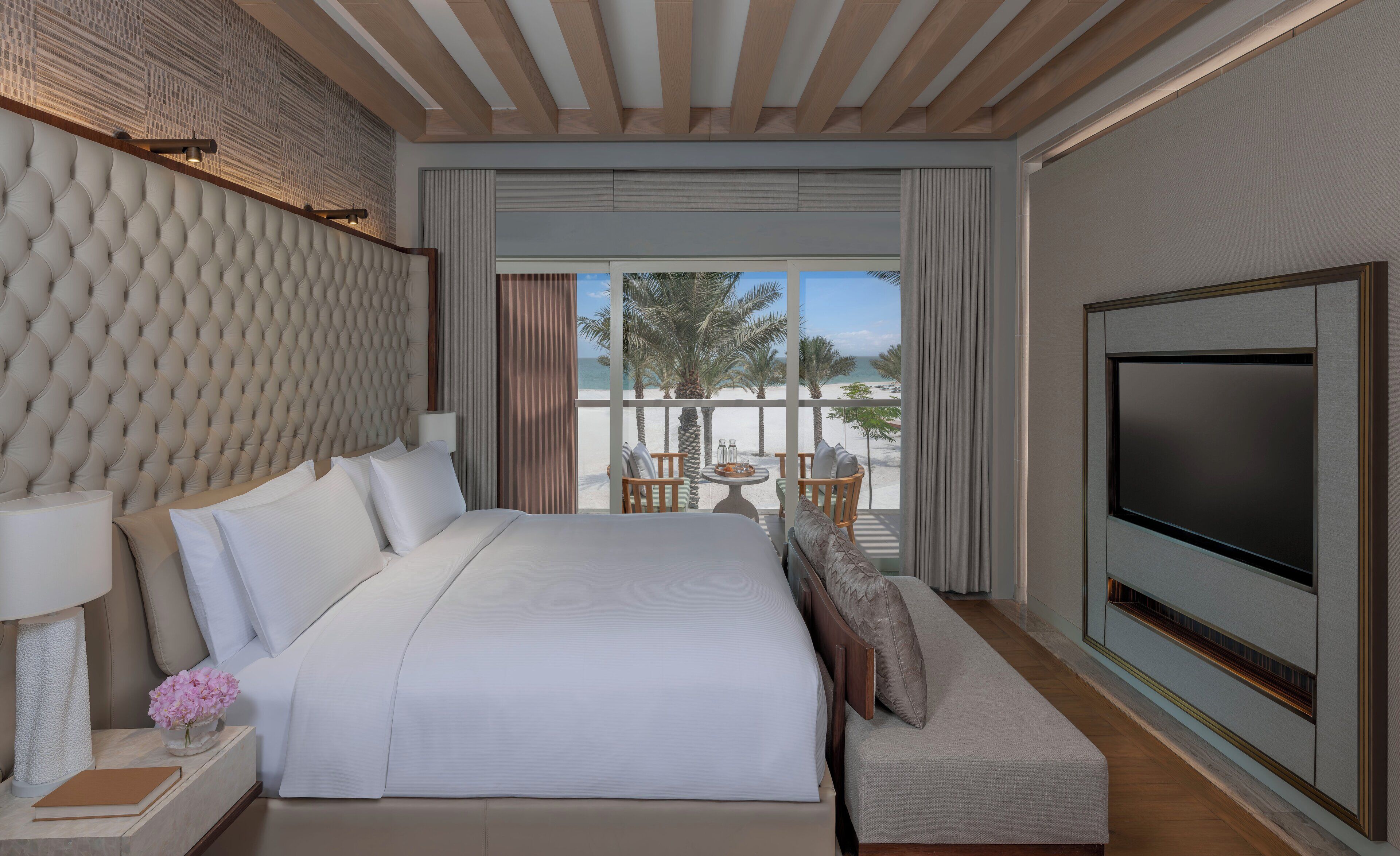 A modern hotel room with a large bed, a TV, and a balcony with a view of the beach.