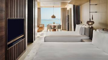 A hotel room with a large bed, a TV, a dining area with a table and chairs, and a view of the sea.
