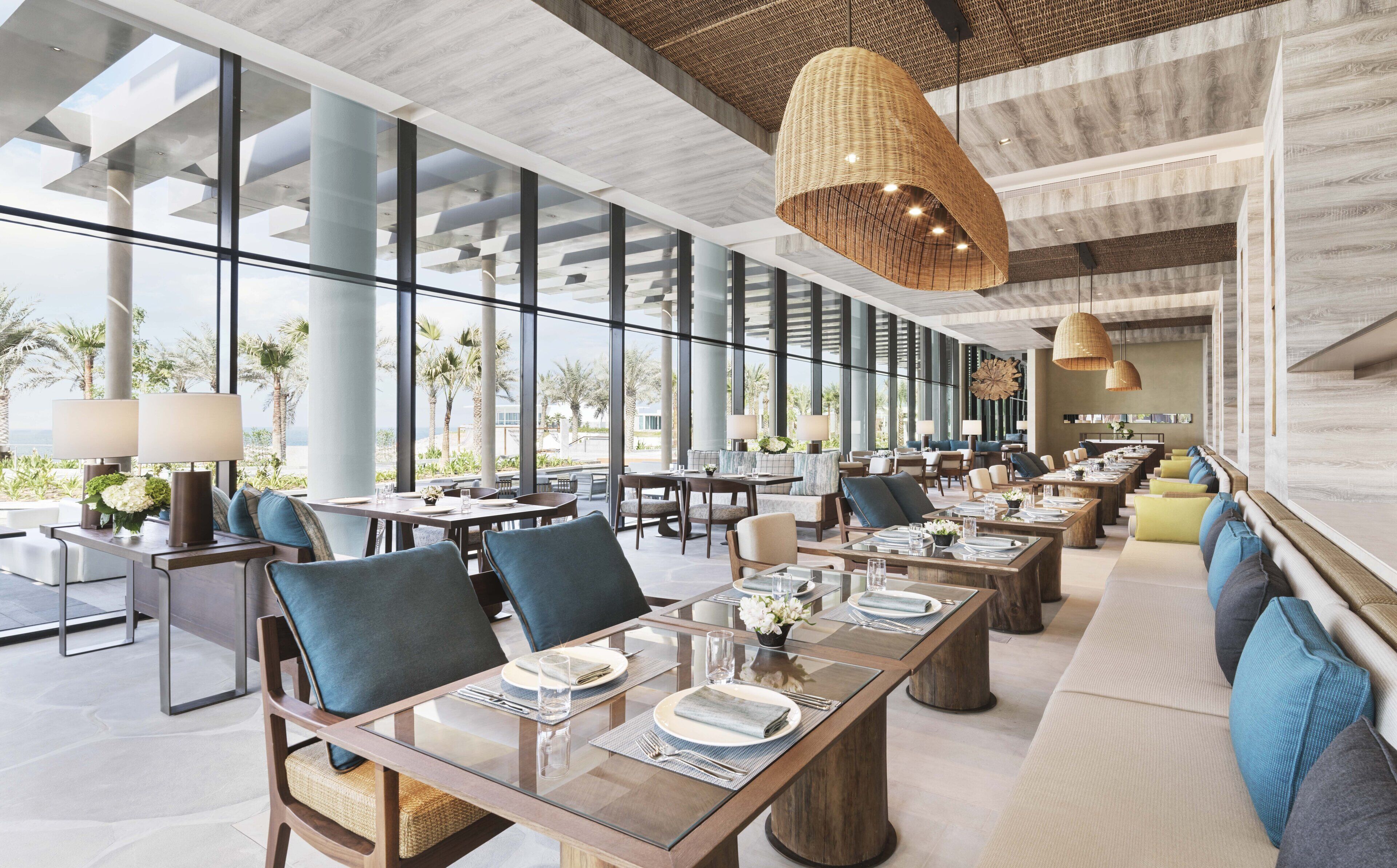 A spacious dining area with large windows, modern furniture, and a view of palm trees.
