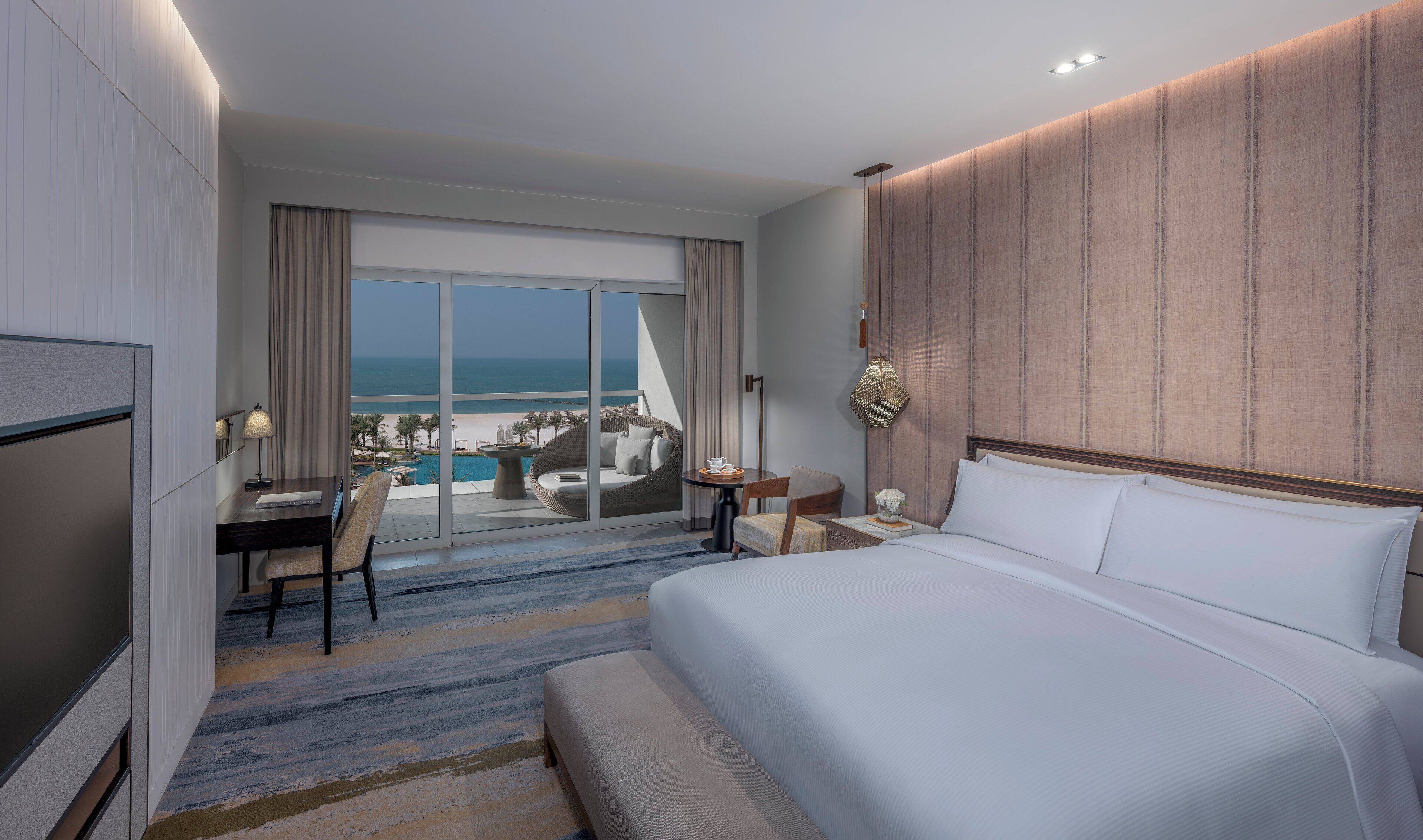 Una camera d'albergo con un letto grande, una scrivania, una sedia e vista sull'oceano.