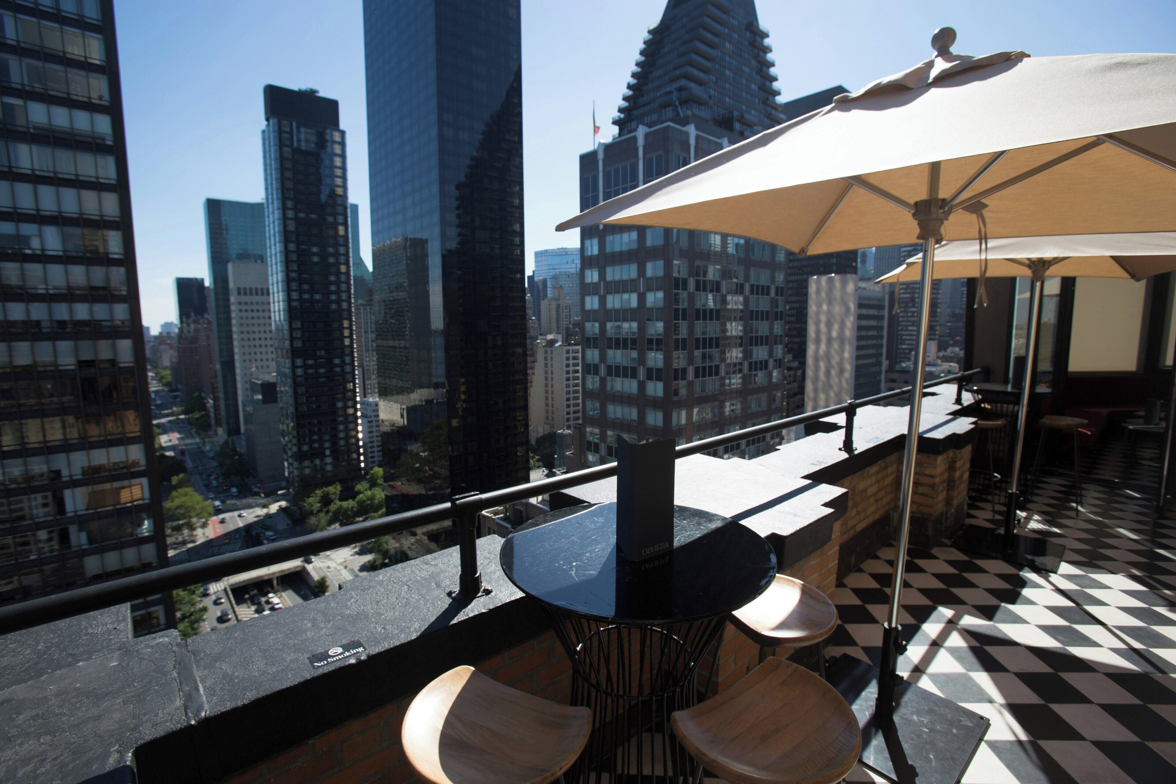 A rooftop bar with a checkered floor, a table with chairs, and a large umbrella.
