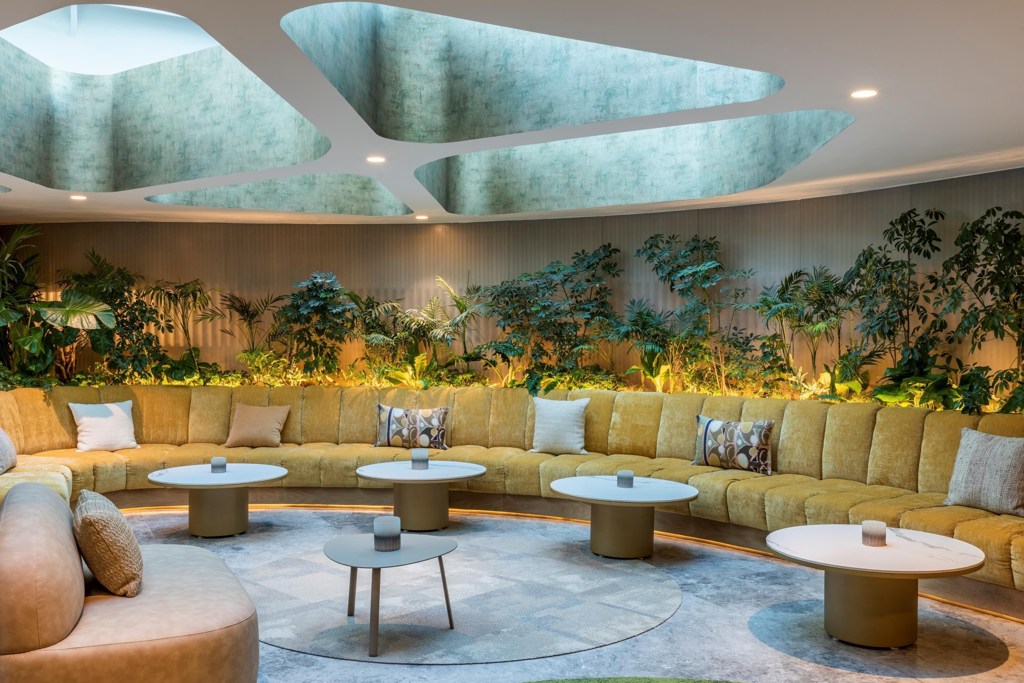 Un espace de détente moderne avec un canapé incurvé, des tables rondes et un plafond orné de motifs géométriques.